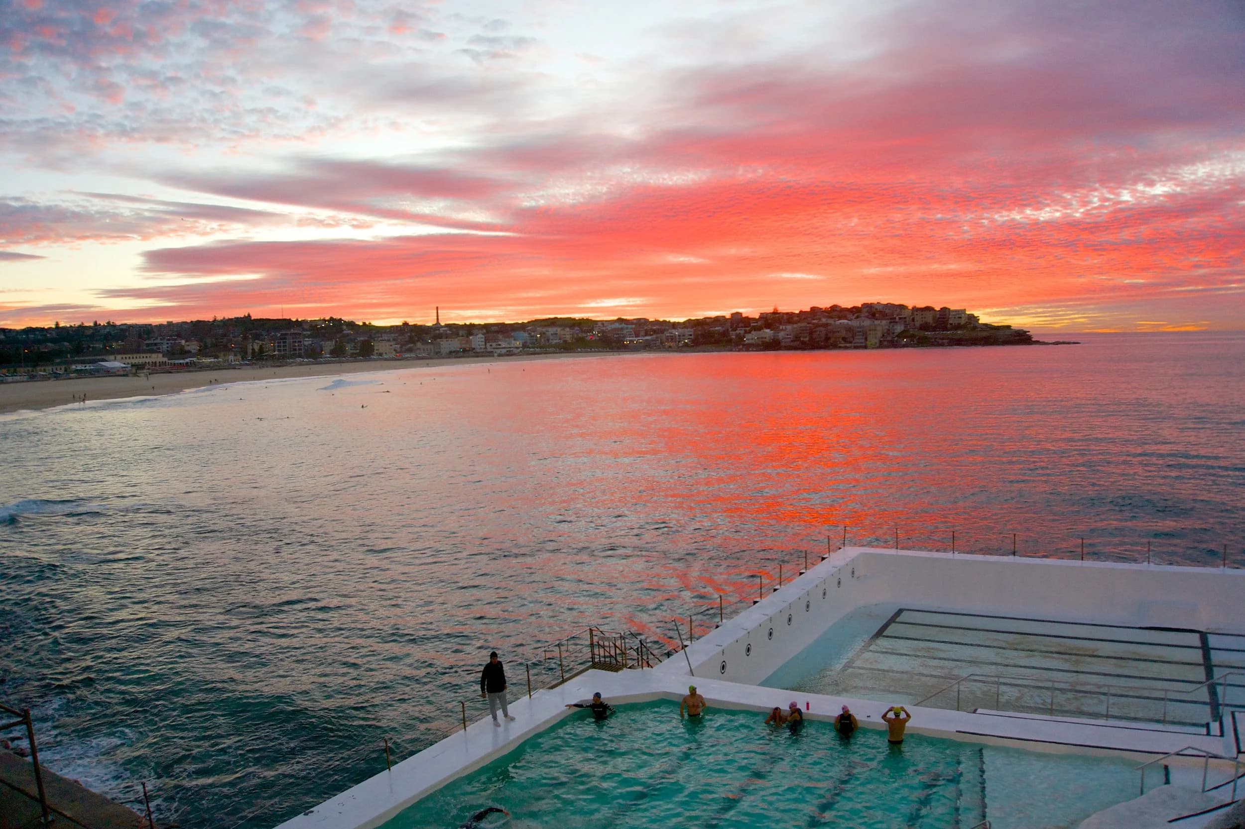 Sunrise over Bondi Beach and the Icebergs ocean pool, with swimmers and the North Bondi headland beyond
